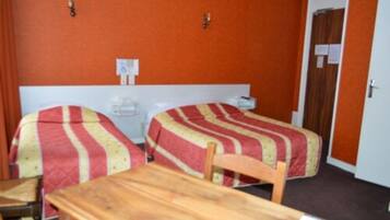 A room with two beds, each with a striped bedspread, a wooden table, and a chair.