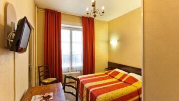 Ein Hotelzimmer mit Bett, Schreibtisch, Stuhl, Fernseher und einem Fenster mit Vorhängen.