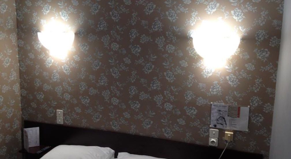 Una camera d'albergo con carta da parati floreale, un letto con lenzuola bianche e due luci fissate al muro.