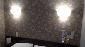 Una camera d'albergo con carta da parati floreale, un letto con lenzuola bianche e due luci fissate al muro.
