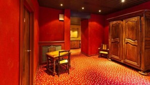 Habitación con paredes rojas, techo de madera y alfombra estampada. Se observa un armario de madera y una mesa con sillas.