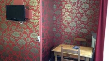 A small room with a floral wallpaper, a wooden chair, a small table, and a mounted television.
