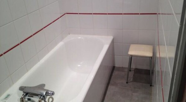 A bathroom with a white bathtub, a small stool, and tiled walls.