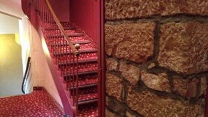 Una escalera con escalones alfombrados en rojo y una pared de piedra.