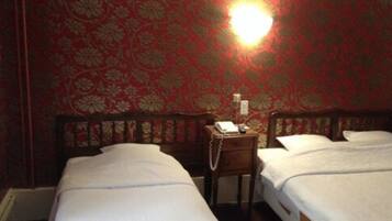 A hotel room with two beds, a nightstand with a telephone, and a wall with a floral pattern.