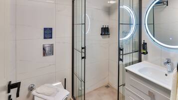 A modern bathroom with a glass-enclosed shower, a white sink, and a mirror with a circular light.