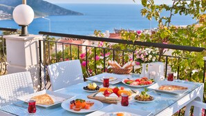 A table set with breakfast items including eggs, toast, and fruit, overlooking a scenic coastal view.