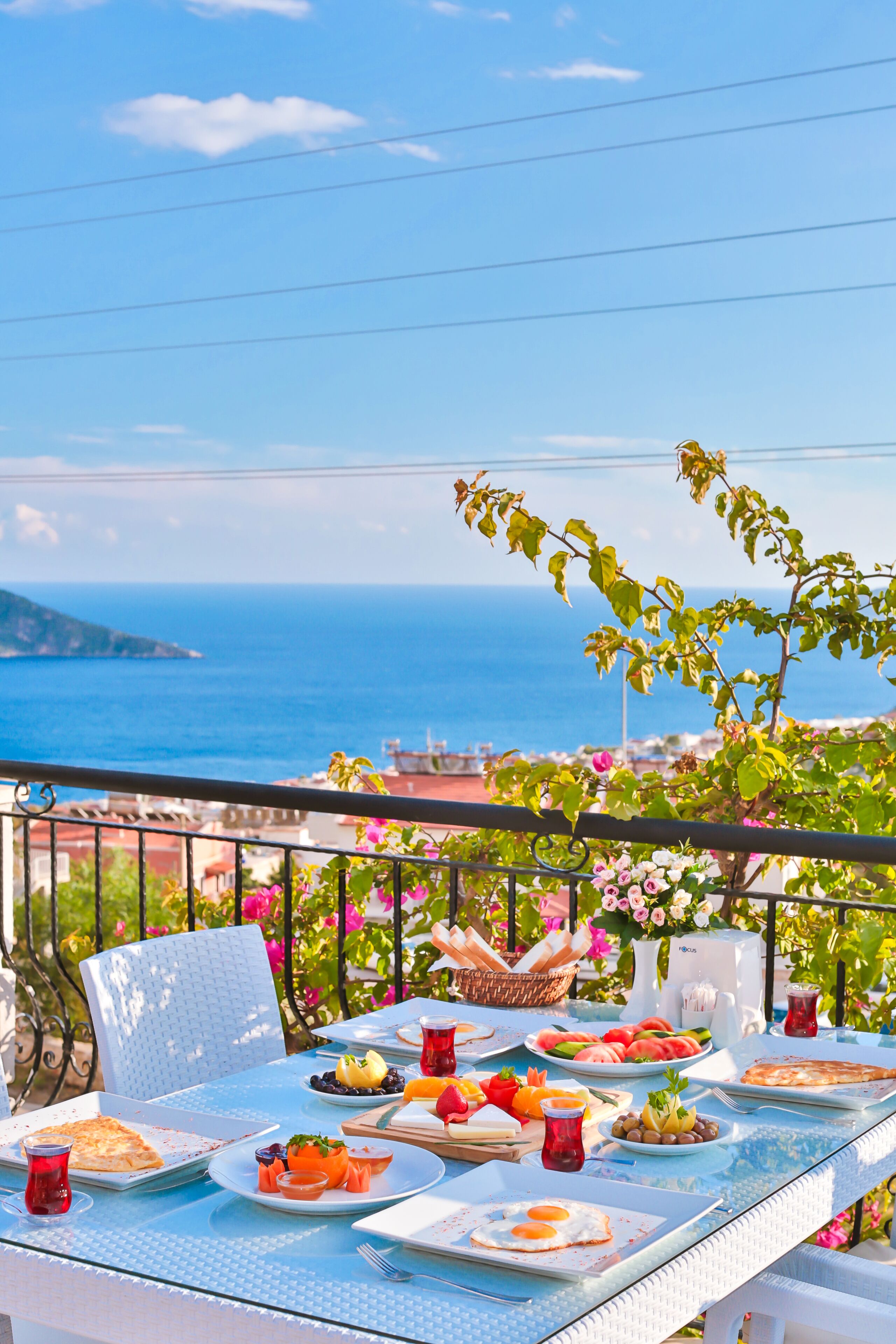 A table set for breakfast with a view of the sea, a chair, and a balcony railing.