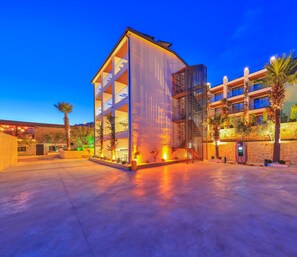 A modern building with multiple floors, large windows, and a parking area with a charging station. - Samira Resort Hotel Aparts & Villas (Kas)