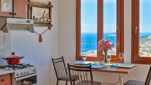 A kitchen with a stove, a red pot, and a window with a view of the sea.