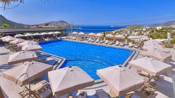 A pool area with sun loungers and umbrellas, surrounded by a clear view of the sea and hills.