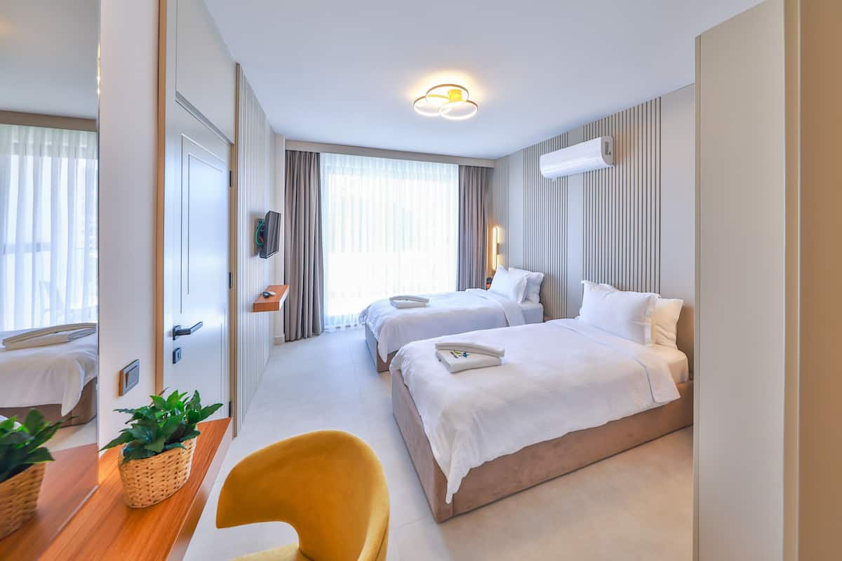 Ein Hotelzimmer mit zwei Betten, einem Fernseher, einem Schreibtisch mit Pflanze und einem gelben Sessel.