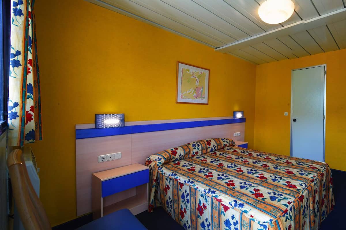 A small room with a bed, a desk, a chair, a television, and a door.