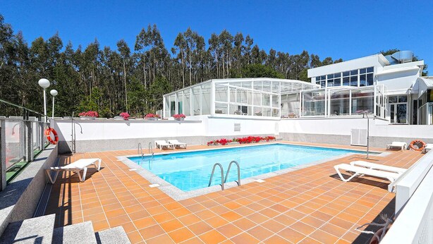 A swimming pool with sun loungers, a glass-enclosed structure, and a view of trees. - Compostela Inn (Teo)
