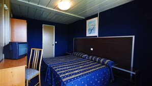 A small, compact room with a single bed, a wooden desk, a chair, a television, and a door. - Compostela Inn (Teo)