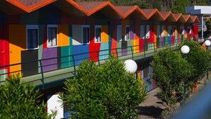 A row of colorful, single-story cabins with a green roof and white railings. - Compostela Inn (Teo)
