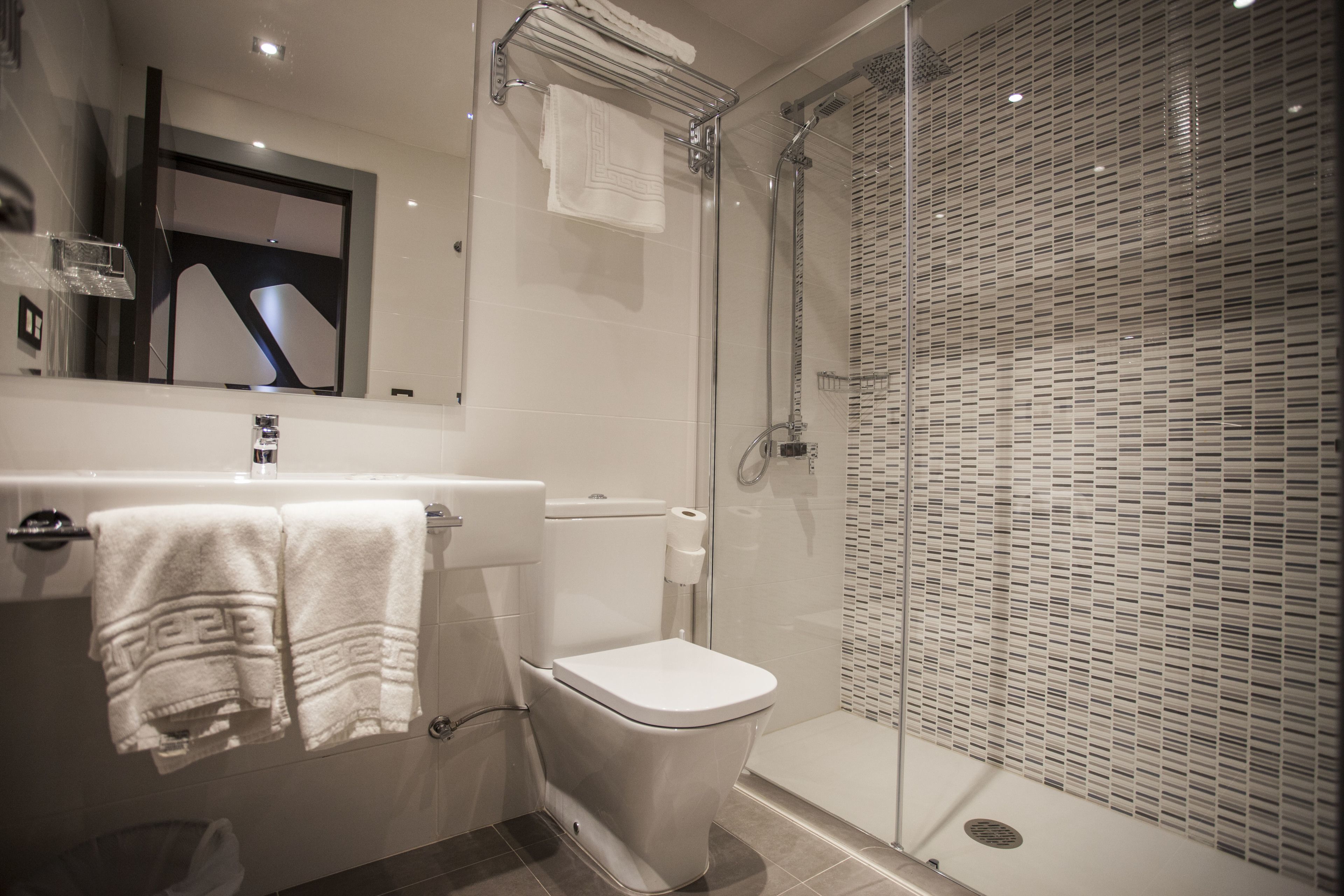 Un baño moderno con ducha envuelta en vidrio, inodoro blanco y lavamanos con toallero.
