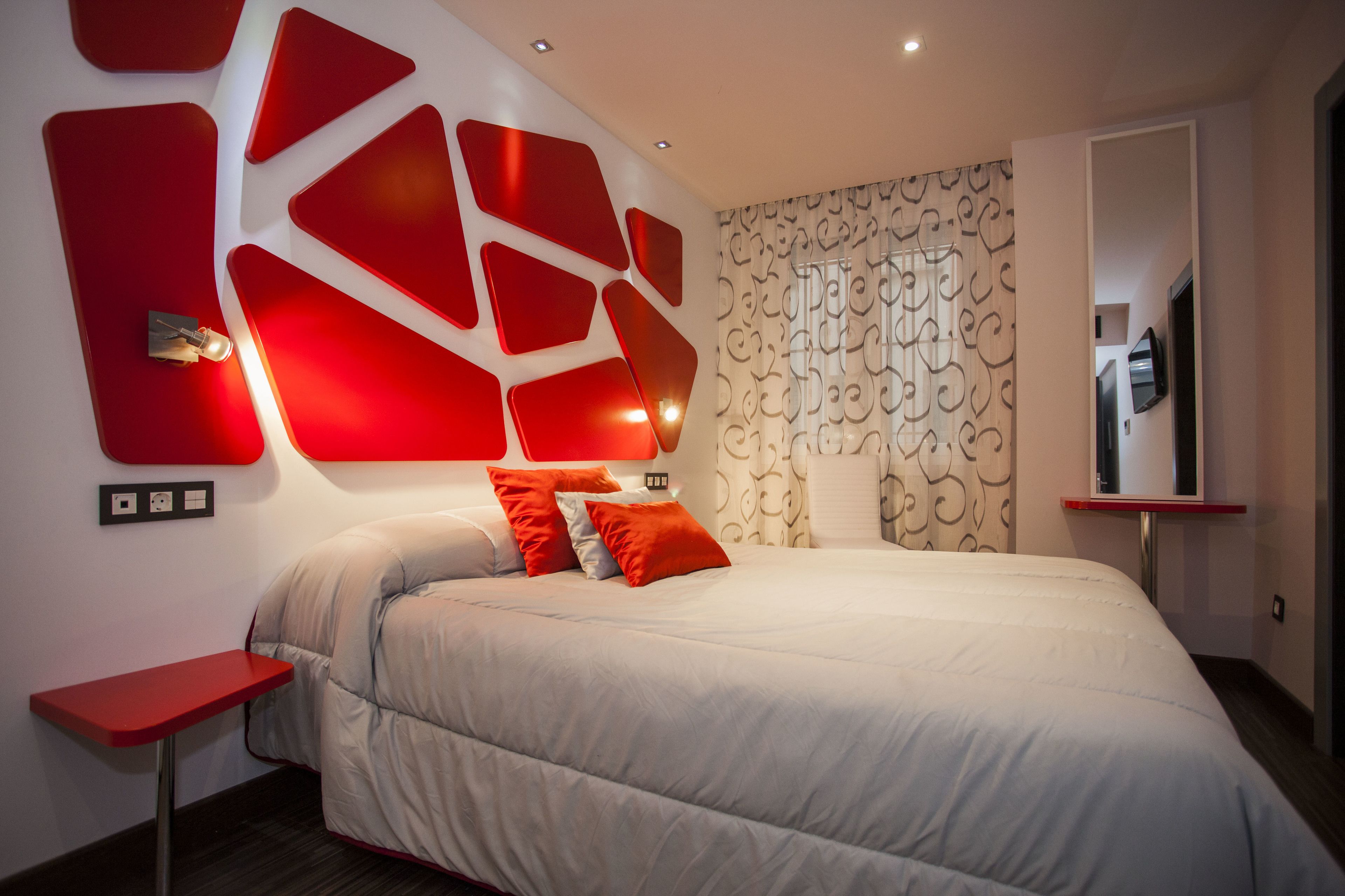 Quarto moderno com uma cama grande, paredes em tons de vermelho e papel de parede estampado.