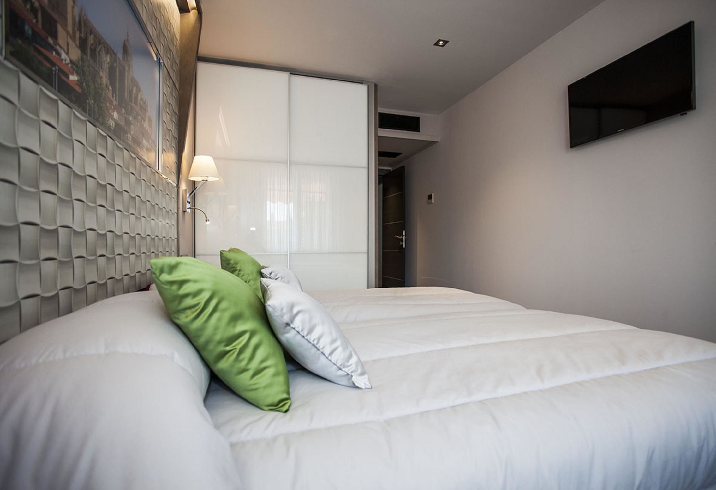 Habitación de hotel con una cama grande, cabecera con diseño texturizado, televisor montado en la pared y un cuadro sobre la cama.