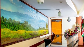 A reception area with a large landscape painting, a reception desk, a floral arrangement, and a flag.