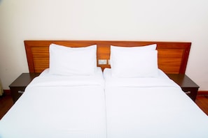 A double bed with a wooden headboard, two white pillows, and a matching white bedspread.