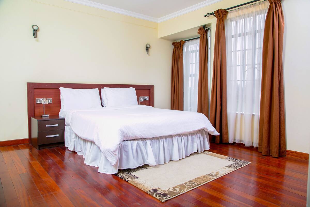 A neatly made bed with a wooden headboard, a bedside table with a lamp, and a patterned rug on a wooden floor.