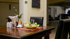 A dining table set with a salad, a bottle, and a vase with flowers.