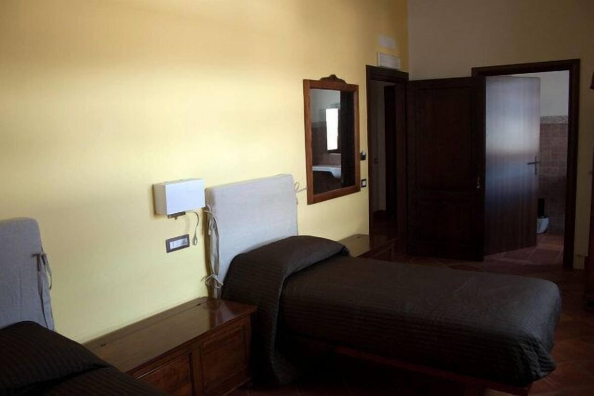 Ein Schlafzimmer mit Bett, Nachttisch, Lampe, Spiegel und einer Tür zu einem anderen Raum.