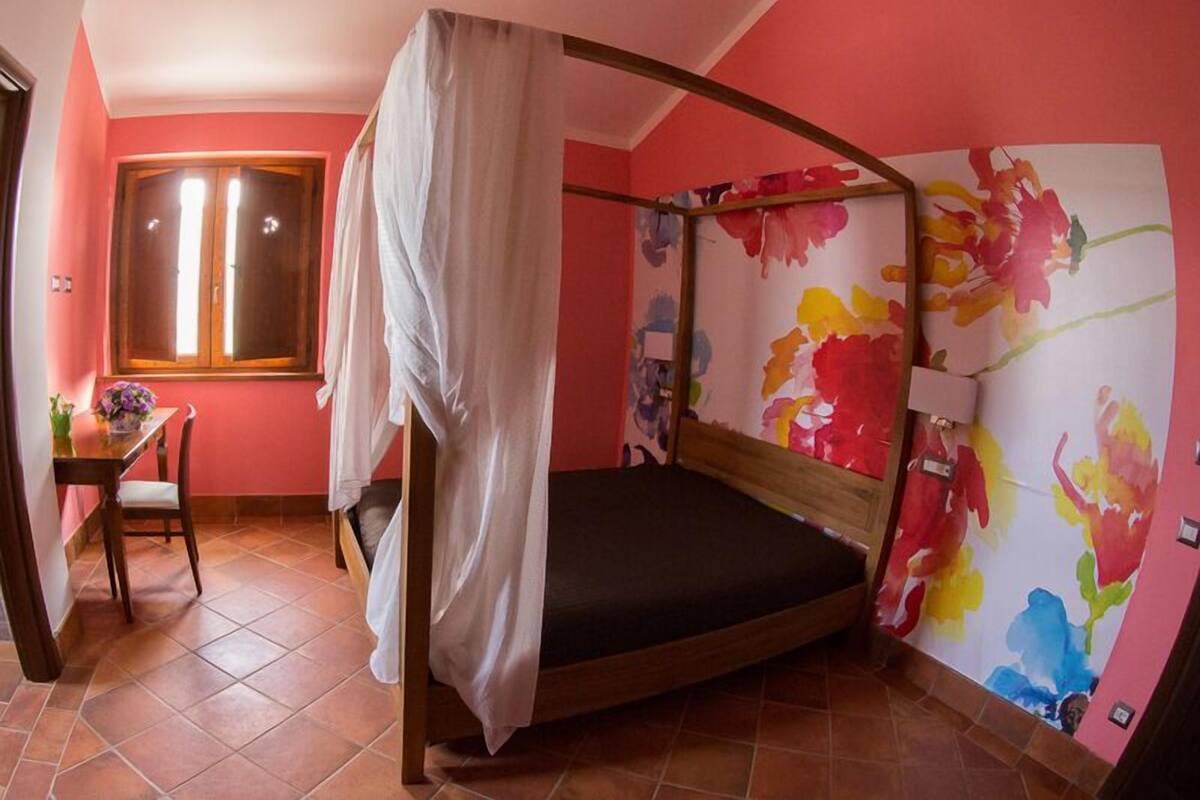 Ein Einzelbett mit Baldachin, ein kleiner Tisch mit Stuhl und ein Fenster mit Vorhängen.