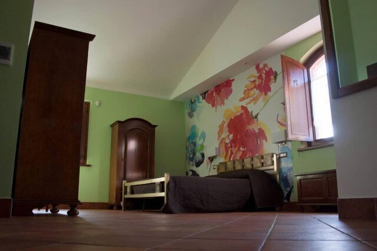 Ein Zimmer mit einem Bett, einem Holzschrank und einem farbenfrohen Wandgemälde.