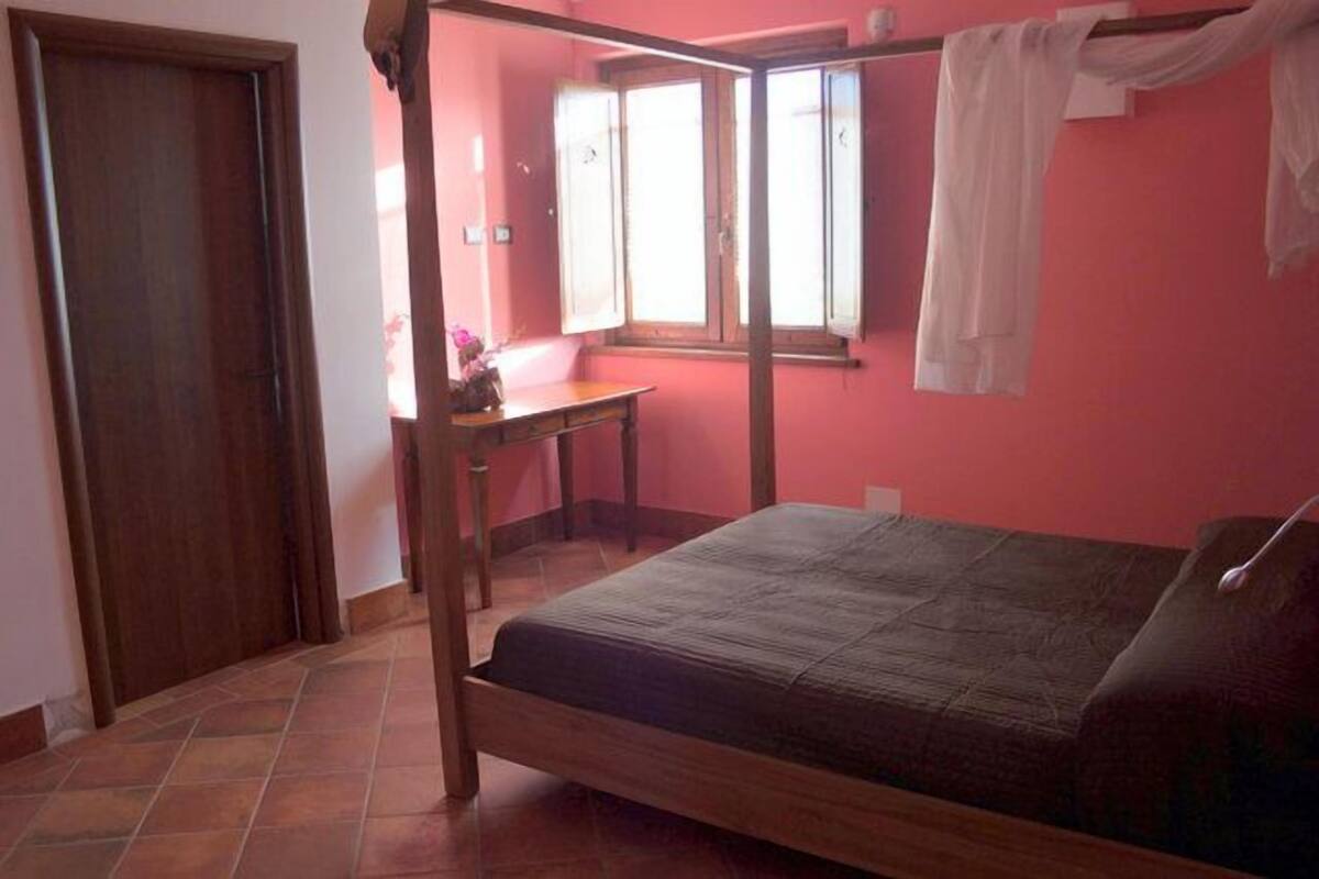 Ein Schlafzimmer mit einem hölzernen Bett, einem Schreibtisch und einem Fenster mit Vorhängen.