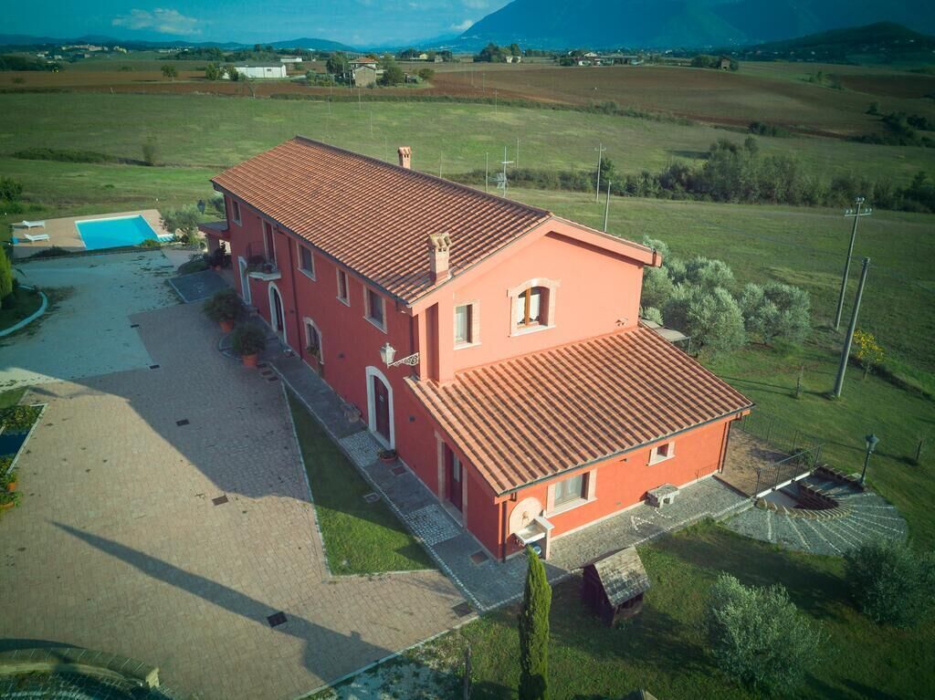 A red villa with a tiled roof, a swimming pool, and a paved driveway.