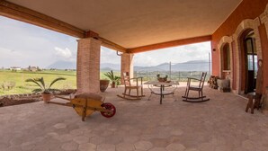 A covered patio with hexagonal tiles, wooden rocking chairs, a small table, and a cart.
