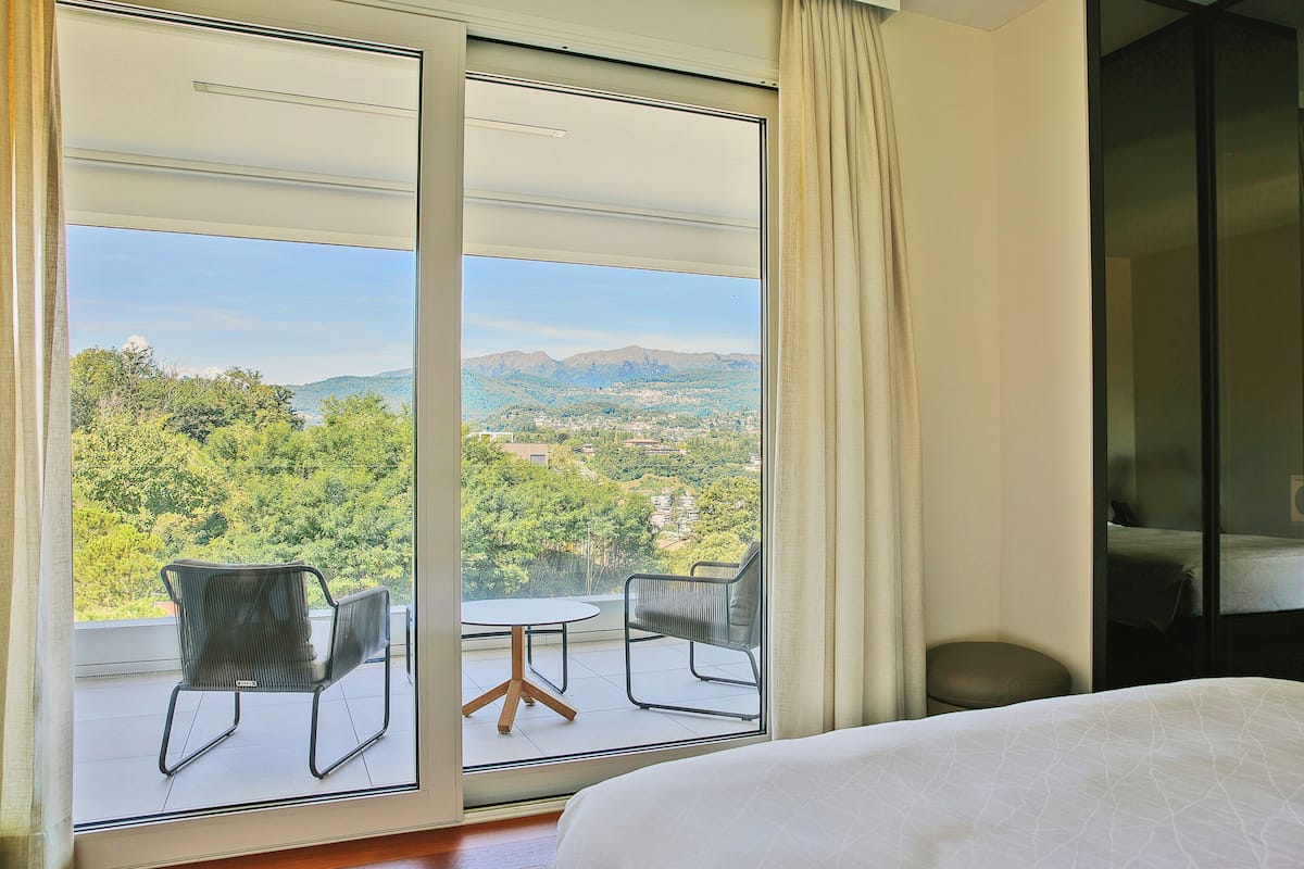 A hotel room with a large sliding glass door leading to an outdoor balcony with a table and chairs, a bed, and a wardrobe.