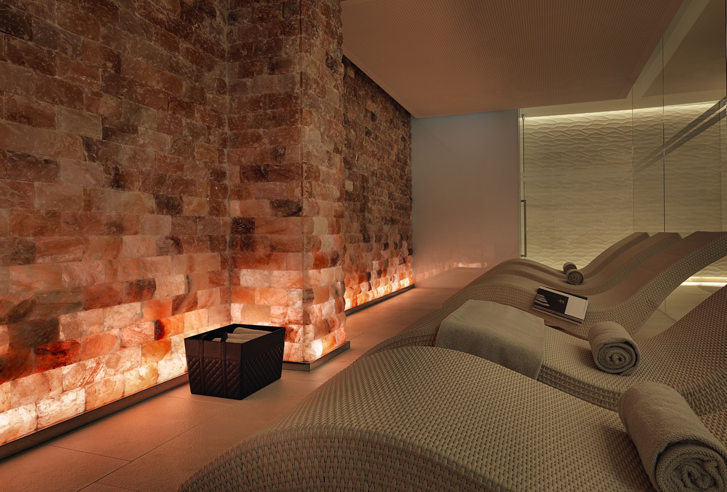 Ein modernes Zimmer mit Backsteinwand, einem Massgebereich inklusive Massageliege und Handtüchern, sowie einer kleinen Holzkiste auf dem Boden.