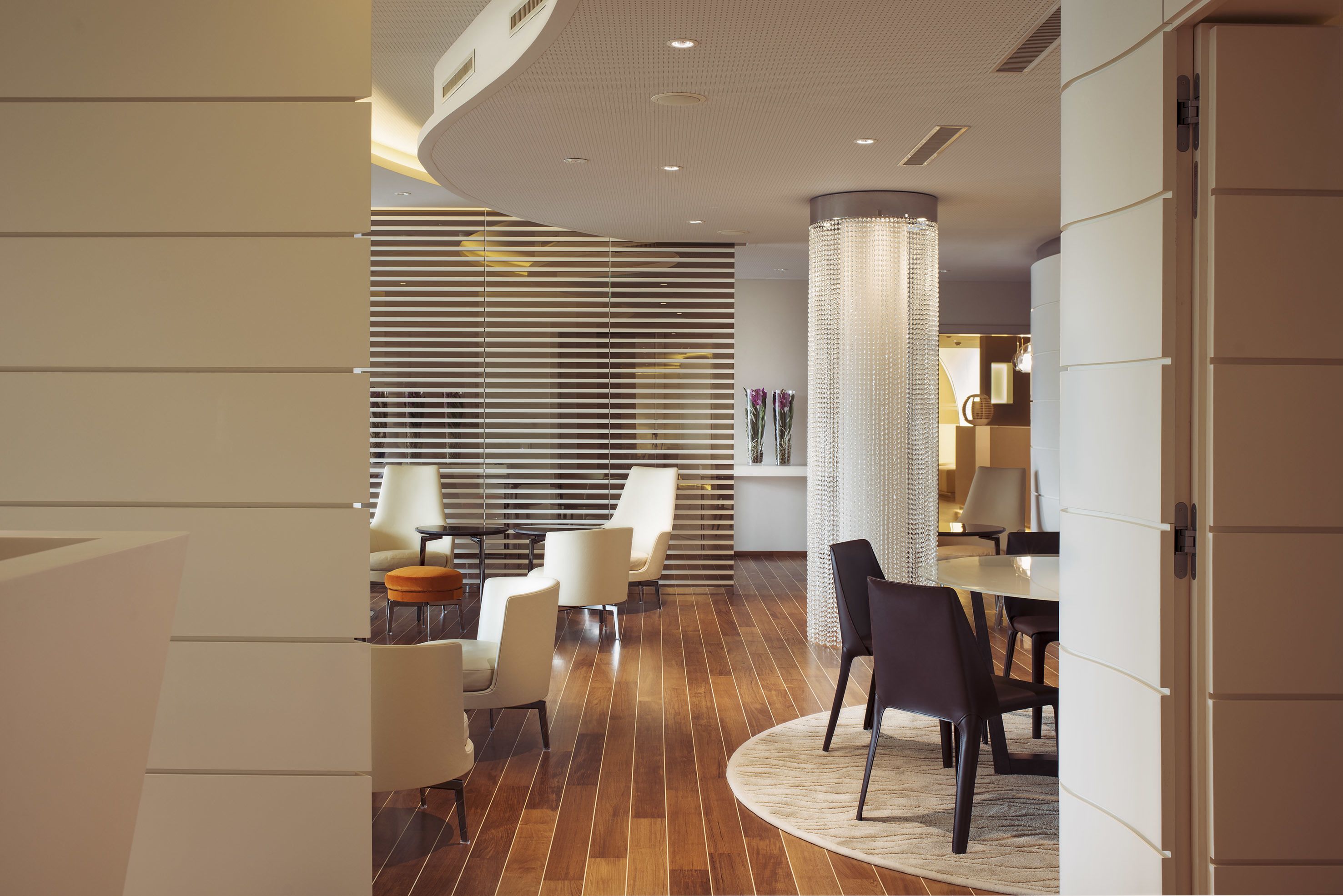 Ein modernes Interieur mit Holzboden, schwarzen und weißen Stühlen, einem runden Tisch und einer dekorativen Säule.