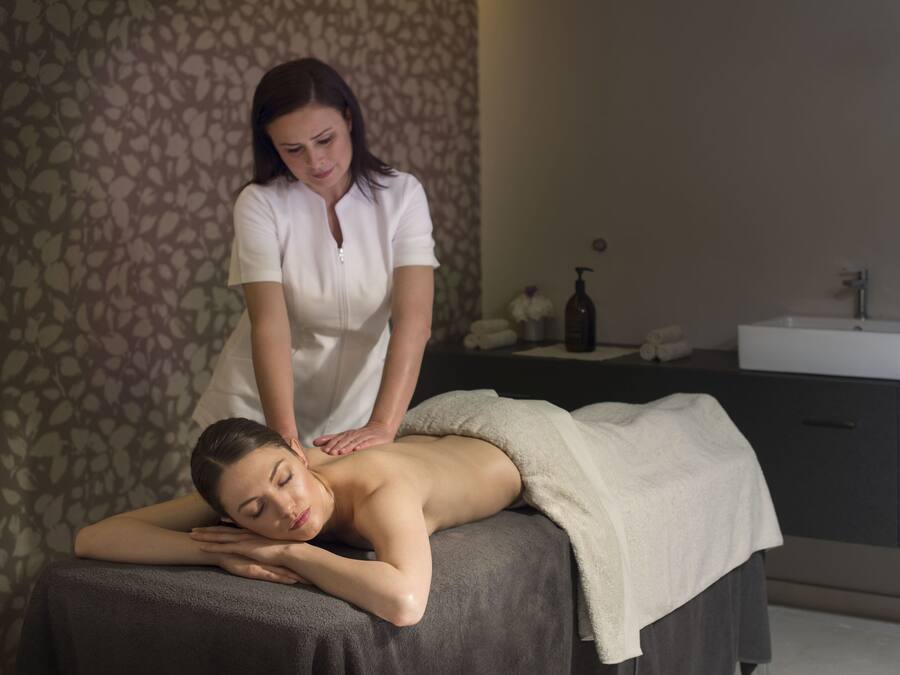 Sessão de massagem em um spa, com parede estampada e pia ao fundo.