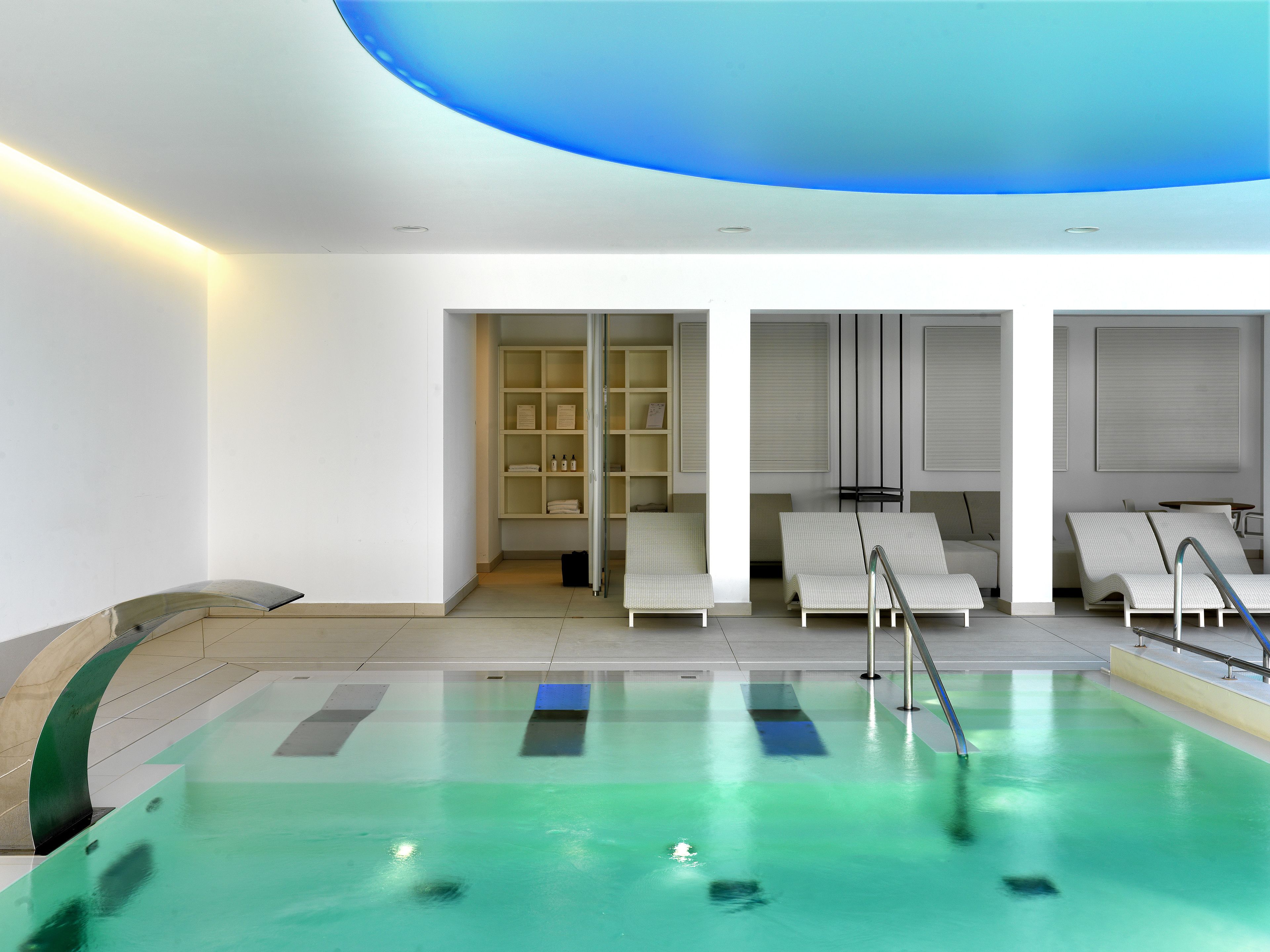 A modern indoor pool area with lounge chairs and a glass-enclosed changing room.