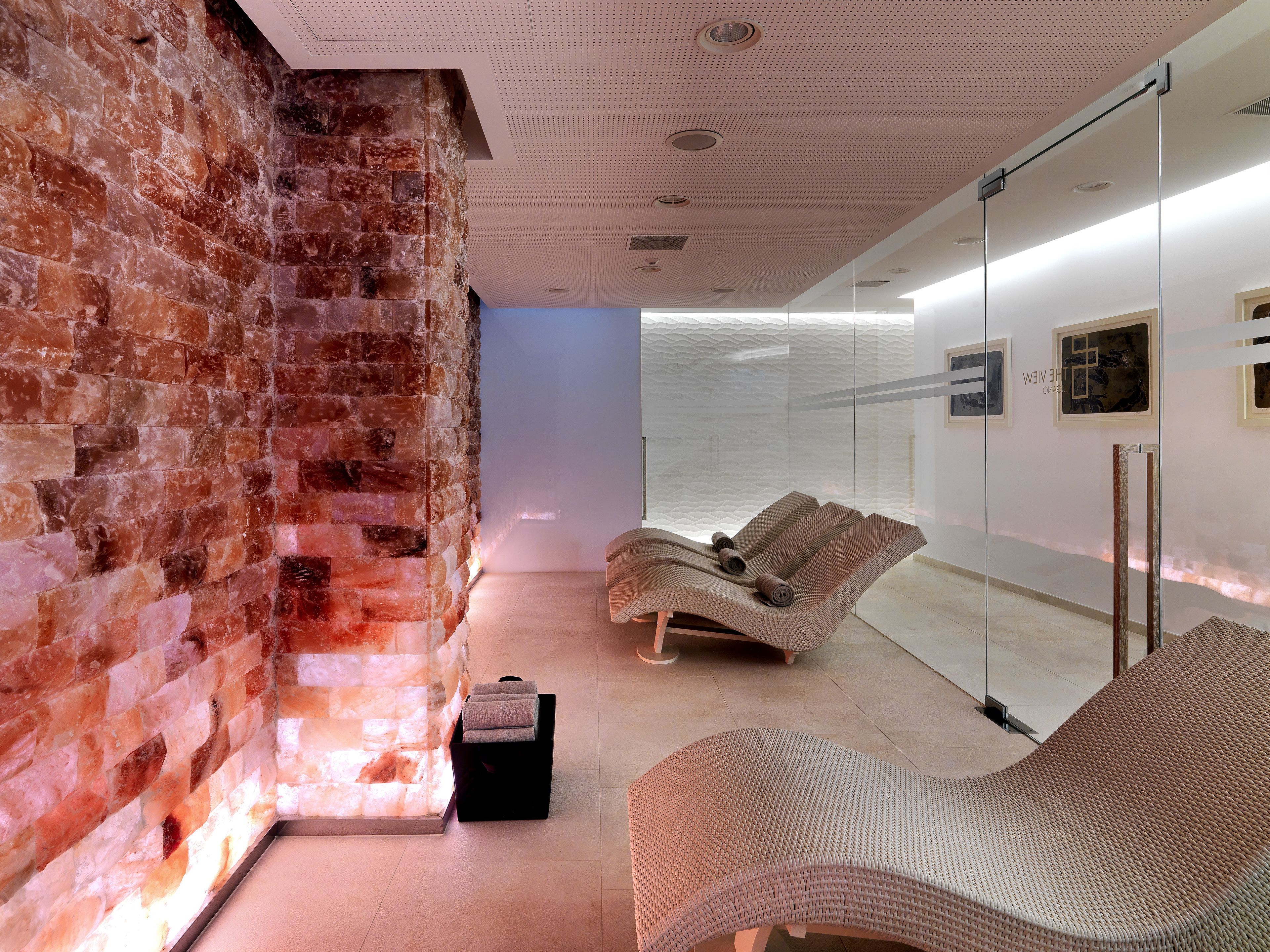 A spa room with a brick wall, a glass partition, and two lounge chairs.