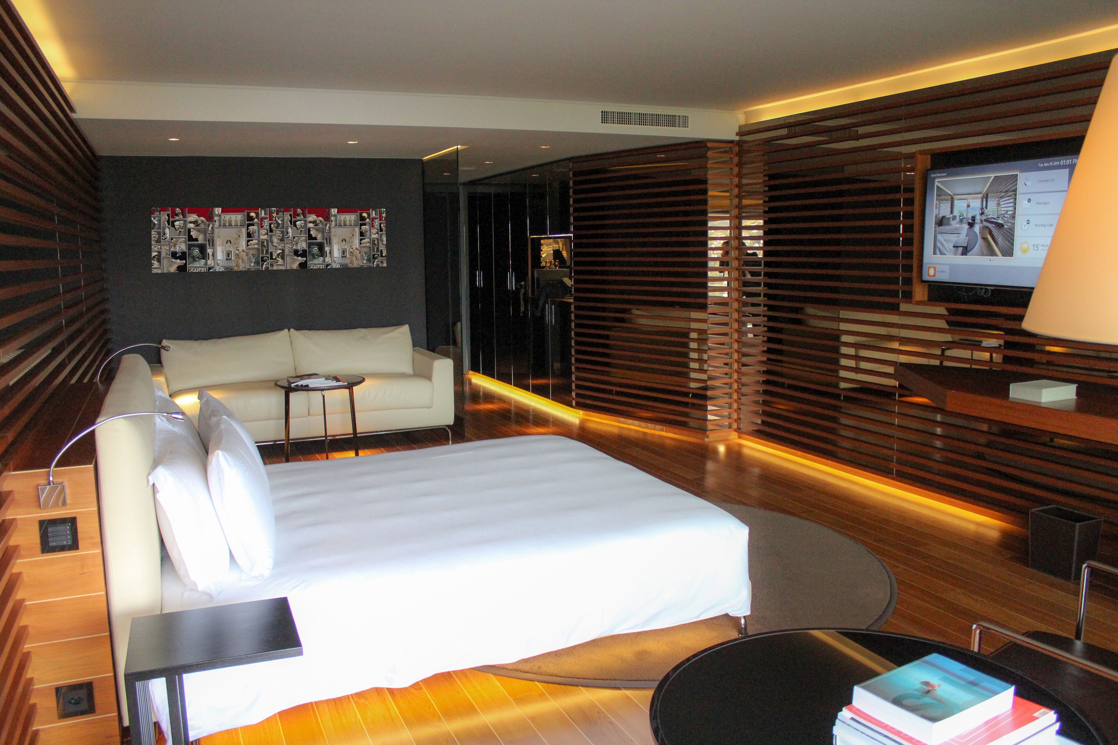 Una habitación de hotel moderna con una cama grande, un sofá, un televisor y un panel de pared de madera.