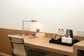 Ein Hotelanfang mit einer Lampe, einer Ablage mit Flaschen und einer Kaffeemaschine sowie einem Stuhl.