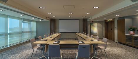 A conference room with a long table, chairs, a projector screen, and large windows.