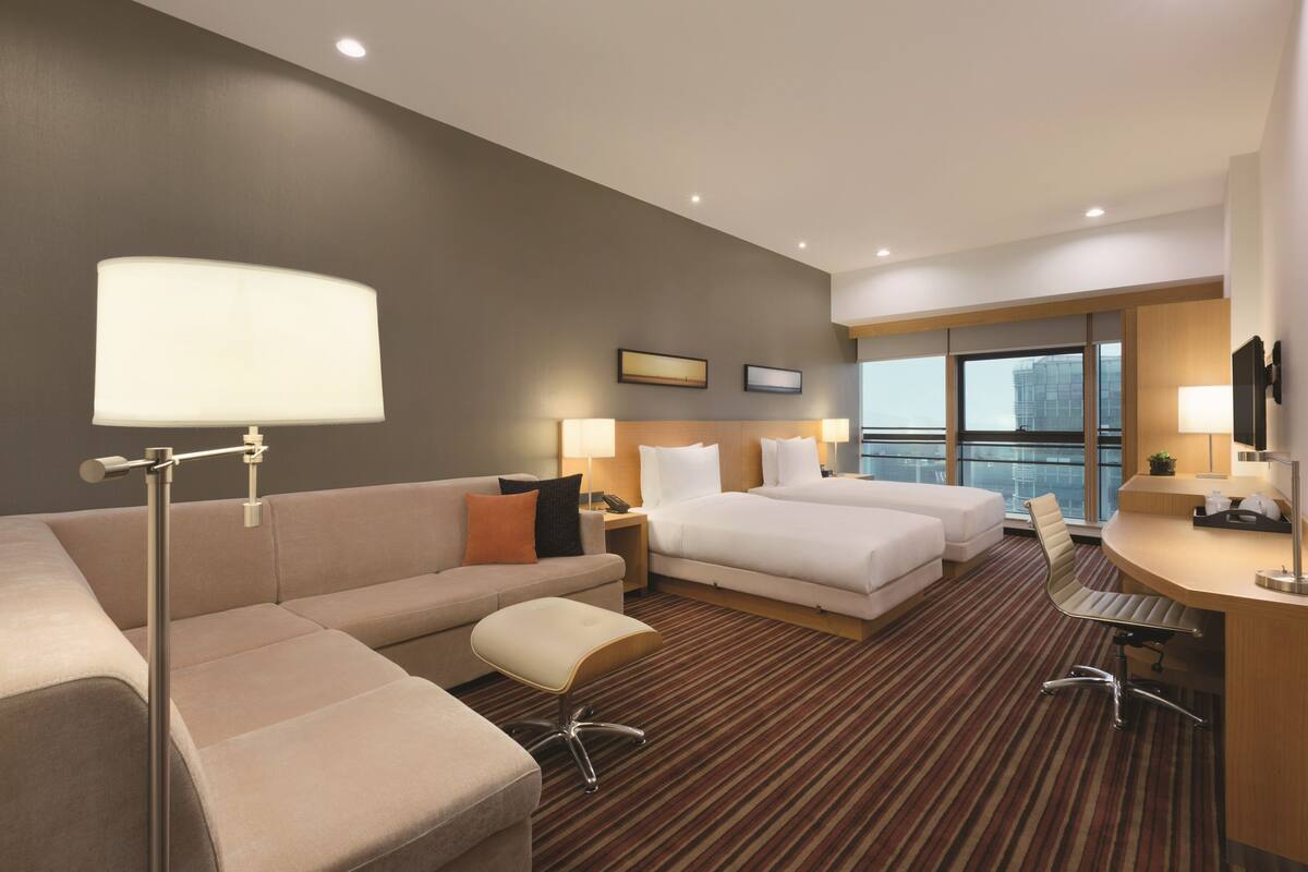 Ein Hotelzimmer mit einer Couch, zwei Betten, einem Schreibtisch und einem großen Fenster.