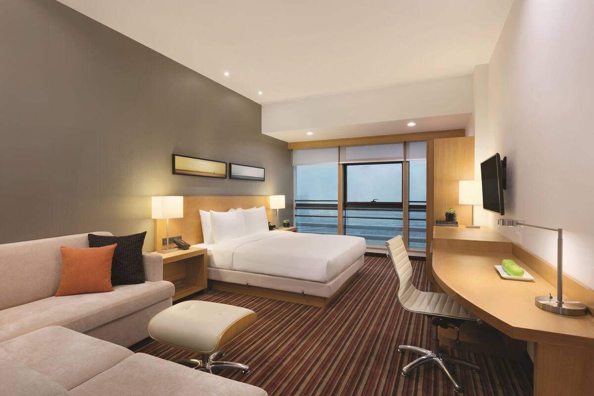 Ein Hotelzimmer mit Bett, Schreibtisch, Sessel, Sofa und Fernseher.
