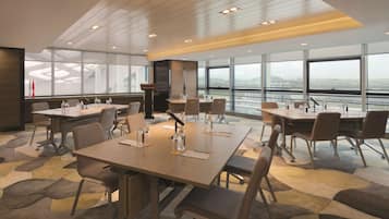 A modern conference room with large tables, chairs, and a view of a cityscape through large windows.