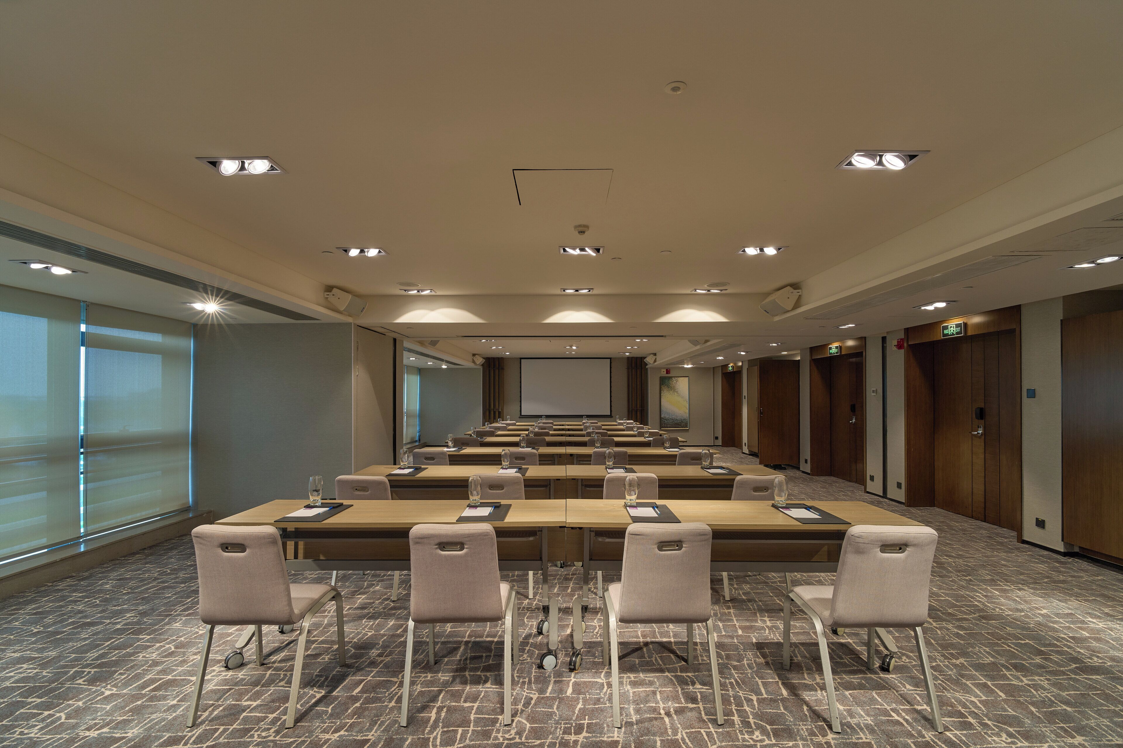 A conference room with a long table, multiple chairs, a projector screen, and a carpeted floor.