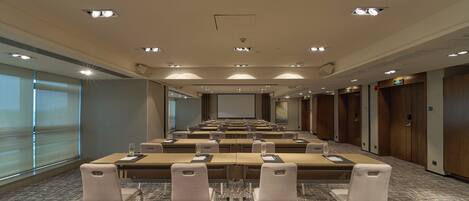 A conference room with a long table, multiple chairs, a projector screen, and a carpeted floor.