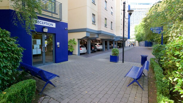 Un'area reception con un cartello blu, l'ingresso di un parcheggio e un vialetto che conduce a un edificio.