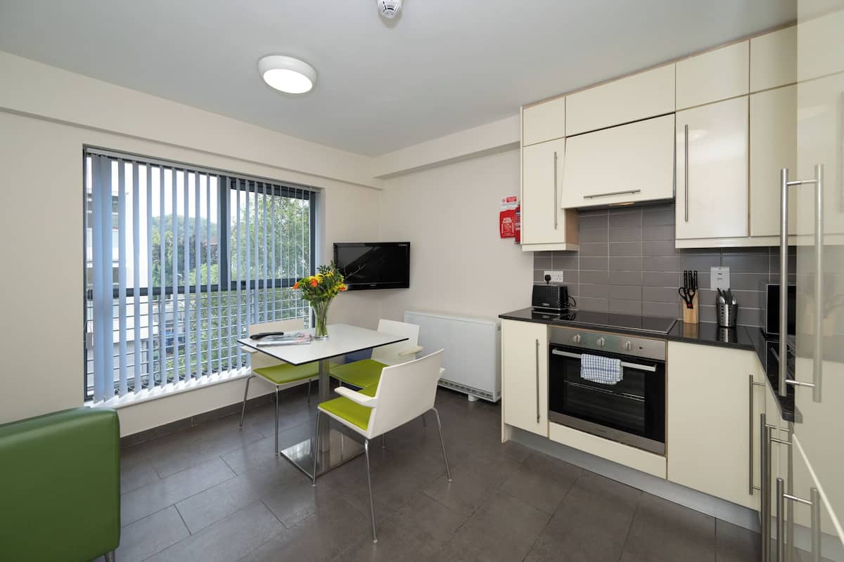 A modern kitchen with white cabinets, a built-in oven, and a dining area with a table and chairs.