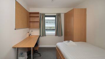 Una habitación de hotel con escritorio de madera, cama, ventana con cortinas y armario.